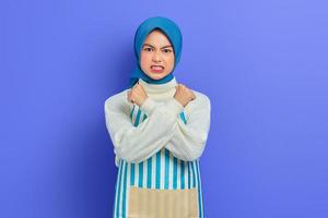 Portrait of angry young housewife woman in hijab and striped apron doing stop gesture with crossed hands isolated on purple background. People housewife muslim lifestyle concept photo