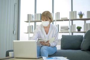 Caucasian senior Businesswoman with mask is working in modern office photo