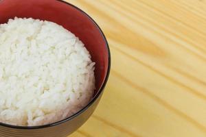 arroz jazmín cocido en tazón blanco sobre mesa de madera y fondo oscuro con espacio para copiar, comida alta en calorías, vista superior. foto