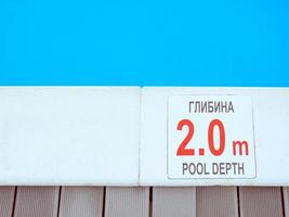 The edge of the swimming pool with the table with information of the depth in English and Ukrainian language. Sport, safety, recreation and relax concept. photo