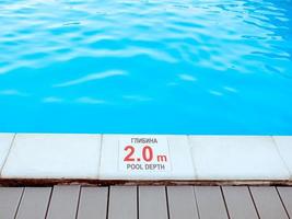 The edge of the swimming pool with the table with information of the depth in English and Ukrainian language. Sport, safety, recreation and relax concept. photo