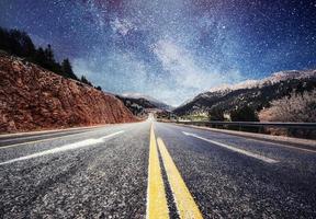 Asphalt road and lonely tree under a starry night sky and the Milky Way photo