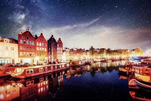 Beautiful night in Amsterdam. Night illumination of buildings and boats near the water in the canal photo