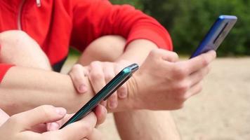 le mani dell'uomo e della donna usano gli smartphone mobili su una spiaggia video