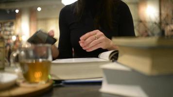 una estudiante con muchos libros en la mesa del café del campus universitario leyendo video