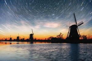 Colorful spring night with traditional Dutch windmills canal in Rotterdam. Wooden pier near the lake shore. Holland. Netherlands. Fantastic starry sky and the milky way. photo