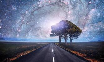 Asphalt road and lonely tree under a starry night sky and the Milky Way. Courtesy of NASA photo