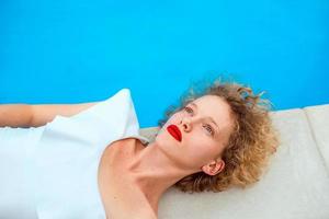 beautiful redhead curly woman in white swimming suit laying by the swimming pool in summer day. Summer, happiness, relax, wellness, recreation concept photo