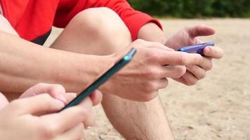 mãos de homem e mulher usam telefones inteligentes móveis em uma praia video