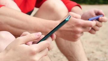 mãos de homem e mulher usam telefones inteligentes móveis em uma praia video