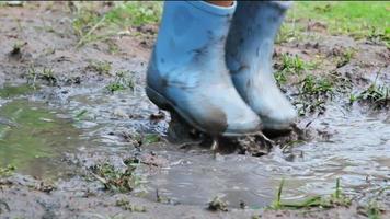 close-up van de voeten van een gelukkig klein meisje in rubberen laarzen die in een plas springen. kindervoeten in de modder video