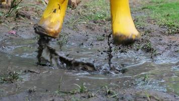 Close-up of the feet of a happy little girl in rubber boots jumping in a puddle. Child's feet in the muddy video