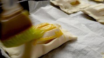 Applying a thin coat of egg yolk with silicone brush on a home-made pastry before baking.  Concept of cooking and baking. Shallow depth of field with selective focus. video