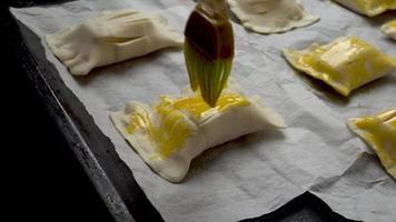 Auftragen einer dünnen Schicht Eigelb mit einem Silikonpinsel auf ein selbstgebackenes Gebäck vor dem Backen. konzept des kochens und backens. geringe Schärfentiefe mit selektivem Fokus. video