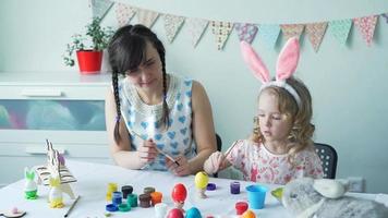 niña pintando huevo de Pascua amarillo con su madre con el cepillo. camara lenta video