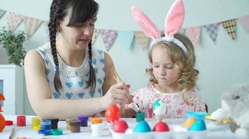 linda niña preparándose para pascua con su madre. ellos pintan huevos de pascua