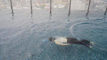 tiro em câmera lenta, jovens mulheres asiáticas nadando na piscina da cobertura, feliz e relaxe com a natação video