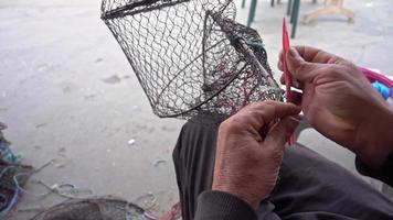 pescador conserta rede de armadilha de peixe dobrável na marinha