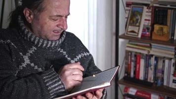Senior Man Writer überprüft seine Notizen im Bibliotheksmaterial