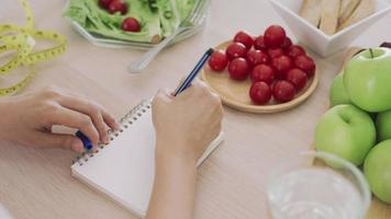 le donne scrivono un programma di dieta nel libro quotidiano per controllare il peso. le donne hanno bisogno di una dieta scegli di mangiare mele verdi ed evitare cibi grassi e spazzatura. concetto di dieta e perdita di peso. video