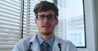 Young male doctor looking at camera and talking while giving online medical consultation video