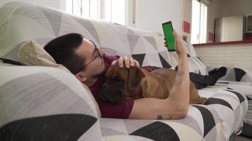 joven con su perro tirado en el sofá mirando su celular, pantalla verde