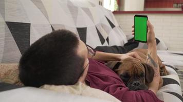 joven con su perro tirado en el sofá mirando su celular, pantalla verde