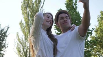junges paar, das ein selfie auf ihrem handy im park macht. lateinischer mann und kaukasische frau