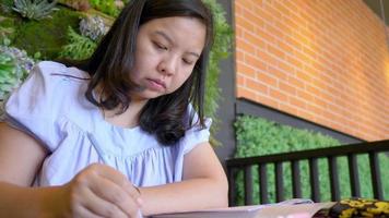 mujer asiática sentada en el escritorio sosteniendo un bolígrafo tomando notas en un libro en el café, mujer de negocios tratando de escribir ideas y planes de negocios de inicio en el café, pensamientos creativos para el cuaderno. creando el concepto de lista video