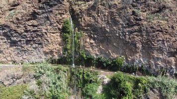 Aerial drone view of people bathing on a high waterfall falling on the road on a sunny day. Anjos waterfall in Madeira Island.. Hot day and people having shower below the waterfall. Travel the world. video