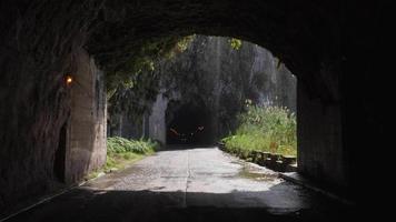 túnel escuro com água pingando no final durante um dia ensolarado. estradas escorregadias e perigosas. ilha da madeira, portugal. viajar com cautela. vida nômade. video