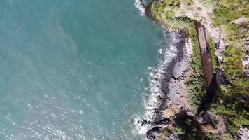 fantastisk flygdrönarevy över havet och klipporna. en bil dyker upp från tunneln och passerar på vägen intill havet. vackert blått havsvatten. resa jorden runt och upptäck vacker natur. video