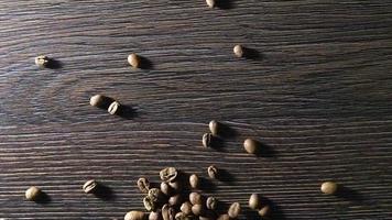 vídeo animado de grãos de café caindo em câmera lenta. grãos de café arábica torrados em um fundo de madeira. o conceito de bebida perfumada de café.