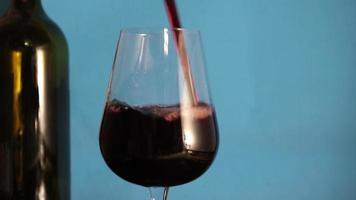 Glas auf dem Hintergrund einer Flasche Rotwein. Traubenwein, der in ein großes Glas fällt. Rotwein in Glas gießen. Vorbereitung für ein romantisches Abendessen. Urlaubskonzept. video