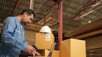 Asian male worker in safety uniform and hard hat using bar code scanner to check shipping orders at parcels warehouse, paper manufacture factory for the packing industry, logistic transport service. video