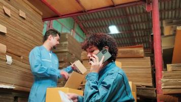 dos trabajadores y colegas de uniformes de seguridad usan computadoras portátiles y teléfonos móviles para verificar las existencias de pedidos de envío en el almacén de paquetes, fábrica de fabricación de papel para la industria del embalaje, servicio de transporte logístico. video