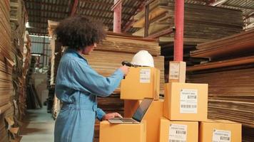 African American female worker in safety uniform using bar code scanner to check shipment orders at parcels warehouse, paper manufacture factory for the packing industry, logistic transport service. video