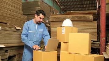 Asian male worker in safety uniform and hard hat using bar code scanner to check shipping orders at parcels warehouse, paper manufacture factory for the packing industry, logistic transport service. video