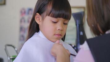 Asian little girl gets her hair cut at a beauty salon by a hairdresser. Hairdresser makes hairstyles for cute little girls. cute little girl cutting bangs. video