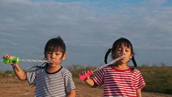 Zwei kleine Schwestern, die im Park Seifenblasen machen. glückliche geschwistermädchen, die bei sonnenuntergang seifenblasen im sommerpark blasen. video