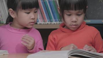 twee schattige kleine meisjes die thuis lezen. schattige zusjes studeren thuis en zijn geïnteresseerd in leren. thuisschool concept video