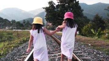 Two cute Asian girls running together on railroad tracks in the countryside against the mountains in the evening. video