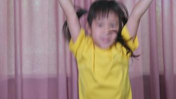 portret van een schattig klein meisje in een geel t-shirt dat vrolijk thuis springt. actieve meisjes voelen vrijheid. concept van gezichtsuitdrukkingen en gebaren video