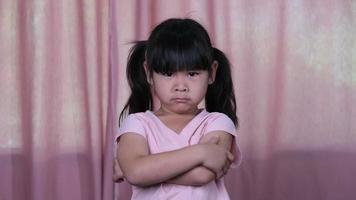 Angry little Asian girl in pink dress showing disappointment and conflict at home.The concept of facial expressions and gestures