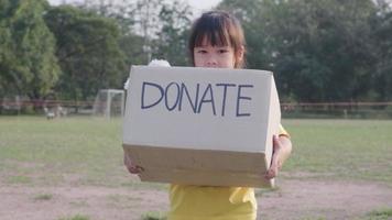 schattig klein meisje met donatiedoos met oude poppen buitenshuis. donatie concept. video