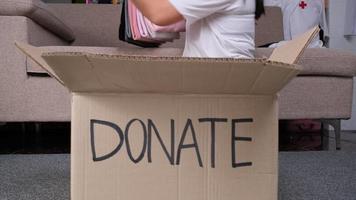 mujer joven poniendo ropa en una caja de donaciones en casa para ayudar a los pobres. concepto de donación. video