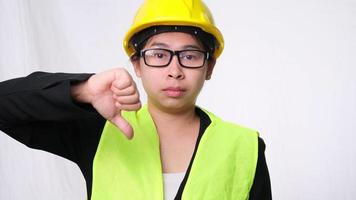 Female technician in helmet standing thumbs down, showing disapproval on white background in studio.