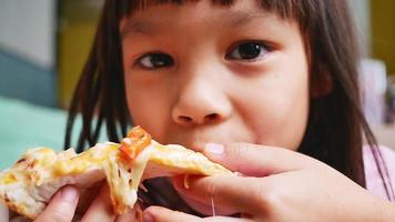süße kleine mädchen, die pizza essen. Hungriges Kind, das zu Hause auf einer Pizzaparty einen Pizzabissen nimmt. Familienurlaubskonzept. video
