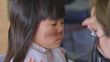 Asiatisches kleines Mädchen lässt sich von einem Friseur in einem Schönheitssalon die Haare schneiden. Friseur macht Frisuren für süße kleine Mädchen. süßes kleines Mädchen, das Pony schneidet. video