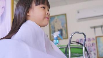 Asian little girl gets her hair cut at a beauty salon by a hairdresser. Hairdresser makes hairstyles for cute little girls. cute little girl cutting bangs. video